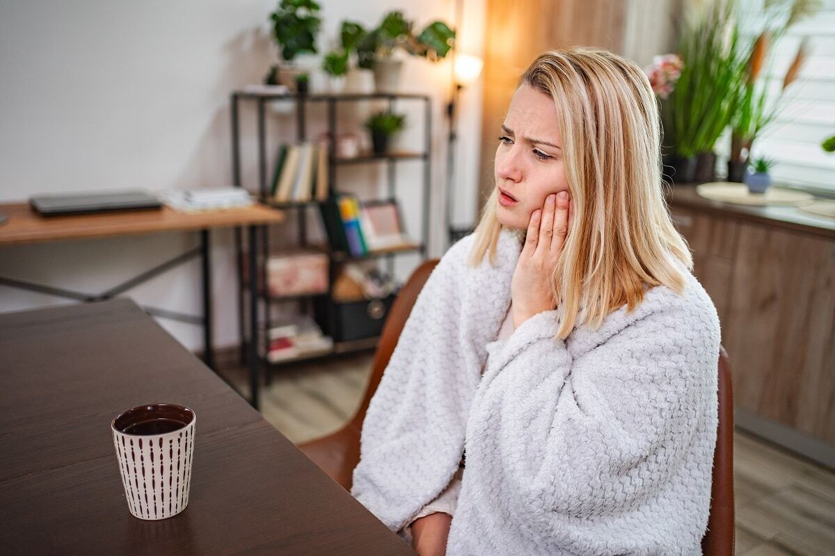 Woman holding her cheek in pain while sitting at a desk, displaying signs of tooth infection.